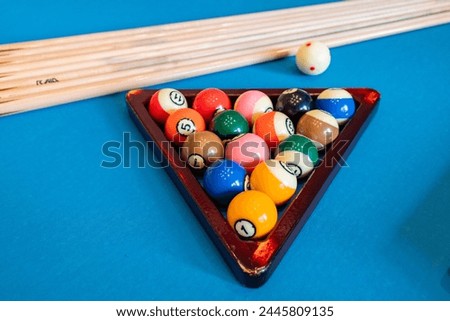 A selective focus shot of numbered billiard balls arranged on a vibrant blue pool table, with cues in the background.