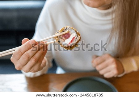 Female hand with chopsticks holds sushi roll. Everyday food. An ordinary raw photo. Trending photos