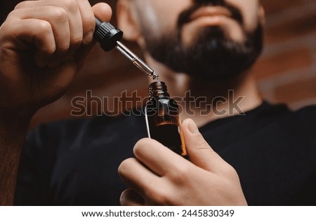 Young man holding pipette with oil for beard hair. Concept spa cosmetic and treatment wellness and natural beauty of skin men. Royalty-Free Stock Photo #2445830349