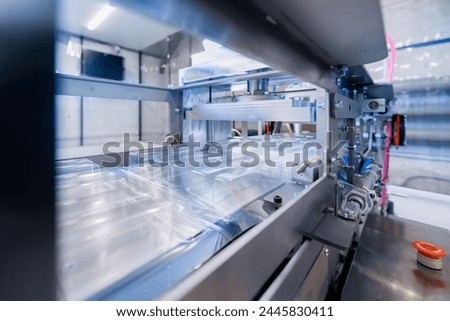 Operation of automatic machine plastic form for kit medical production. Closeup of roller blue toning, with sun lighting effect. Royalty-Free Stock Photo #2445830411
