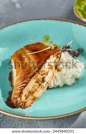 Pan-seared halibut in Unagi sauce with creamy rice served on a turquoise dish, against a textured gray background.