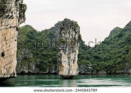 A precarious rock formation in Ha Long Bay, standing tall yet fragile, amidst serene waters