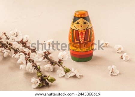 Wooden toy souvenir stylized as a Tatar girl next to flowering branches of forsythia and cherry plum on a gray background. Mass production. Navruz holiday concept.