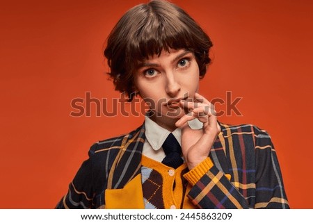 student with short hair posing in stylish checkered blazer on orange background, college girl