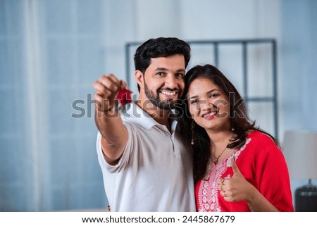 House Ownership. Young Indian Couple Showing Keys And Holding Cardboard Box in new home