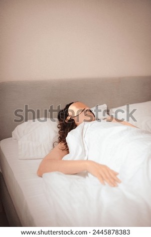 woman in beige silk sleep mask sleep in bed in hotel. Improving sleep quality Royalty-Free Stock Photo #2445878383