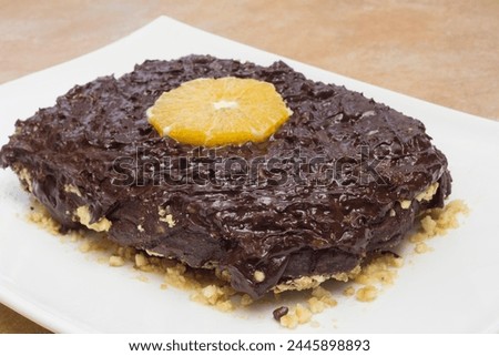 A sumptuous chocolate dessert topped with a fresh orange slice, presented on a white plate against a rustic countertop, highlighting a delightful contrast of colors and textures with a hazelnut base. Royalty-Free Stock Photo #2445898893
