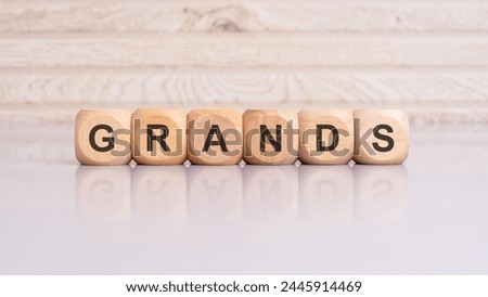 wooden cubes displaying the word 'GRANDS' arranged on a glossy gray surface, with a reflection and wooden background