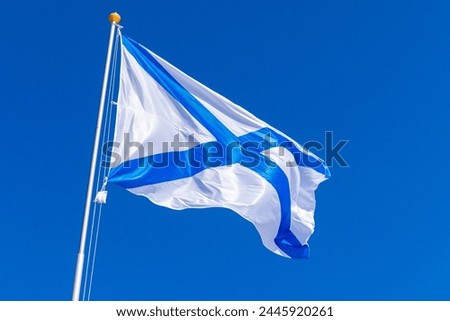 Ensign of the Russian Navy is waving on wind under blue sky, also known as the St. Andrews flag. This is the stern flag of the ships of the Russian Imperial Navy and the Navy of the Russian Federation Royalty-Free Stock Photo #2445920261