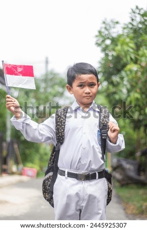 indonesian boy in indonesian school uniform holding flag during independence day. proud elementary school students with the Indonesian flag outdoors
