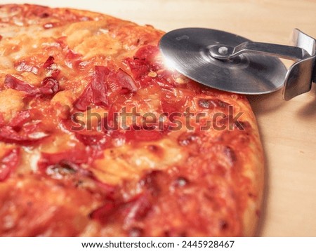 Cooked pizza with spicy chilly peppers on wooden tray and round pizza cutter knife. Italian style fast food for quick cooking. Popular product.
