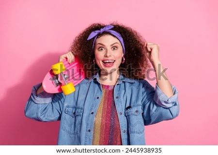 Photo of excited lucky lady dressed denim outfit rising fist holding penny board empty space isolated pink color background