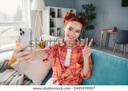 Portrait of charming positive lady sit sofa hold smart phone make selfie demonstrate v-sign pastime apartment indoors