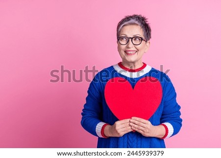 Photo of pretty lovely retired woman wear stylish clothes hold red paper card heart shape empty space isolated on pink color background