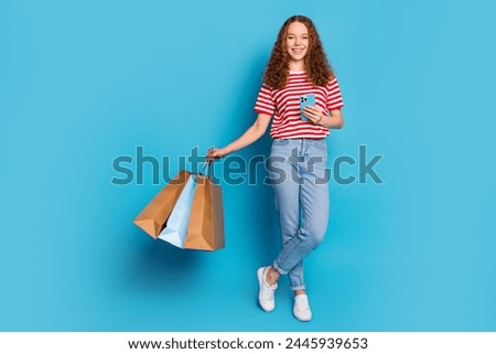 Full size photo of positive girl wear stylish t-shirt denim trousers order new clothes with smartphone isolated on blue color background