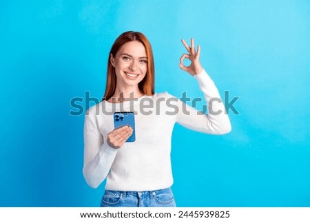 Photo portrait of attractive young woman hold device show okey dressed stylish white clothes isolated on blue color background