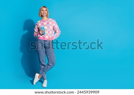 Full size photo of optimistic woman dressed colorful sweater hold smartphone look at offer empty space isolated on blue color background