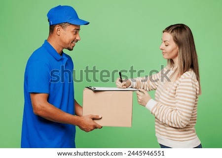 Happy delivery guy employee man wears blue cap t-shirt uniform workwear work as dealer courier hold give blank cardboard box package woman to sign isolated on plain green background. Service concept