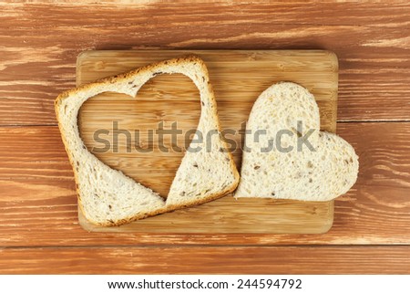 Slice of cereal toast bread with cut out heart shape on wooden cutting board Royalty-Free Stock Photo #244594792