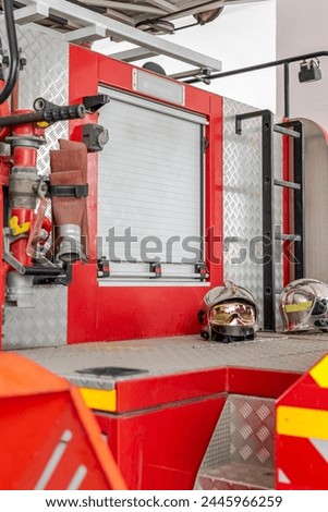 A firefighters truck with two helmets exposed outside near a ladder and a closed curtain. Selective focus with blurred fire hose in foreground. Red colored and yellow stripes. 