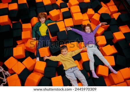 Happy children lying in dry pool with soft cube in entertainment center Royalty-Free Stock Photo #2445970309