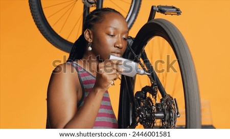 Knowledgeable repairman using specialized glue to recondition broken bicycle chain, orange studio background. Cyclist hobbyist applying adhesive on bike parts during inspection process Royalty-Free Stock Photo #2446001581