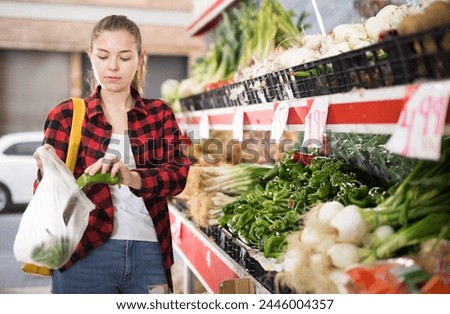 Young positive beautiful woman choosing fresh pepper at grocery section of supermarket