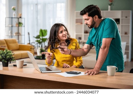 Happy young Indian married couple sit on table calculate expenses use easy online banking service at home