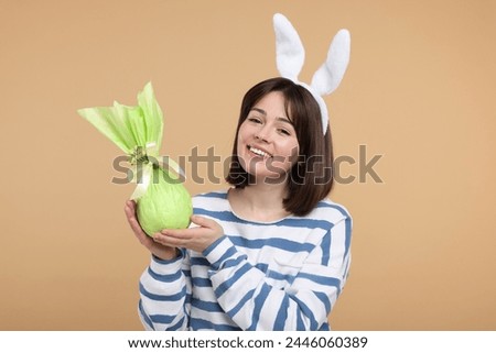 Easter celebration. Happy woman with bunny ears and wrapped egg on beige background