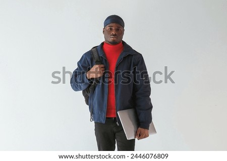 Silver colored laptop in hand. Black man in cap is in the studio against white background.