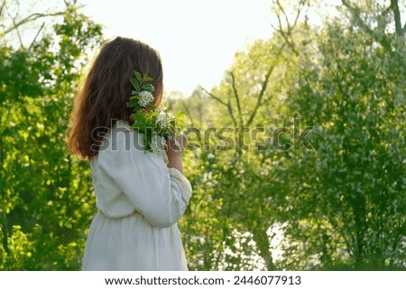girl in rustic white dress with bird cherry tree flower bouquet outdoor, natural green background. concept of youth, romance, dreams, love. gentle lovely image. spring season