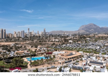 Aerial photo of the town of Benidorm in Spain showing a drone view of a camp site with many motorhomes and caravans on the camping site on a sunny day with mountains and apartments in the background