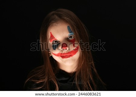 Halloween clown girl portrait on dark background , close-up. Cute child girl with clown face makeup wearing black hoodie. Halloween make-up concept