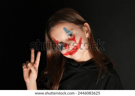 Halloween clown girl portrait on dark background , close-up. Cute child girl with clown face makeup wearing black hoodie. Halloween make-up concept