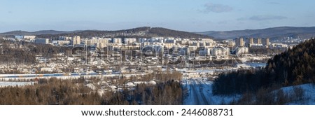 Tynda city, Amur region, Siberia, Russia. Winter panoramic city landscape. In the distance are residential buildings and hills. In the middle ground there is a railway. In the foreground is a road. Royalty-Free Stock Photo #2446088731