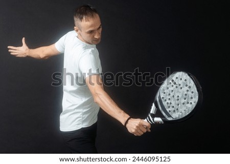 Portrait of man playing paddle tennis in position to hit a backhand ball black isolated background. Front view.
