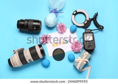 Composition with greeting card, photographer's equipment and Easter decor on blue background