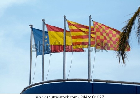 European, Spanish, Catalan and Tarragona flags flutter in the wind on a blue structure under a cloudless sky