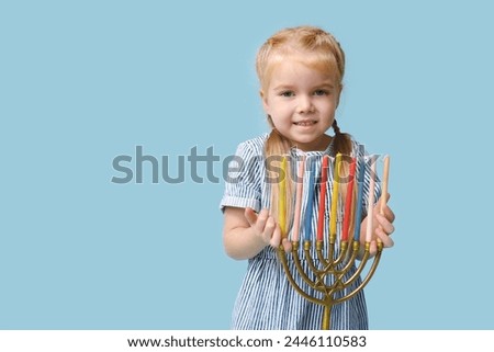 Cute happy little girl with menorah on blue background. Hanukkah celebration