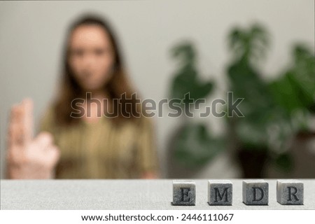 Letters EMDR written on grey stone cubes blocks. Female looking at therapist fingers in blurred background. Eye Movement Desensitization and Reprocessing psychotherapy treatment concept. Royalty-Free Stock Photo #2446111067