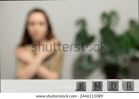 Letters EMDR written on grey stone cubes blocks. Female touching and tapping her shoulders in blurred background. Eye Movement Desensitization and Reprocessing psychotherapy treatment concept. Royalty-Free Stock Photo #2446111089