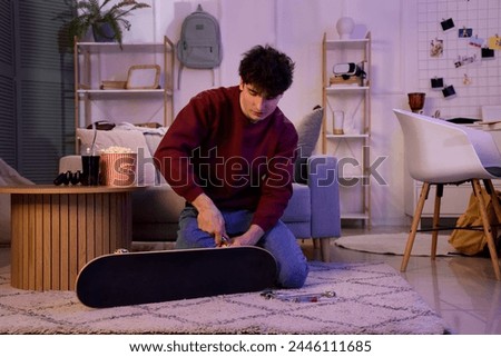 Male student repairing skateboard at home in evening
