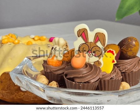 Photo of Easter sweets. These include chocolate bunnies, eggs and a chocolate chicken. Furthermore, a cake is present in the background.