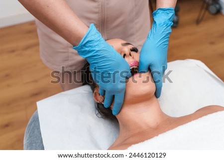 Therapist performs precise TMJ therapy on relaxed patient's jawline Royalty-Free Stock Photo #2446120129