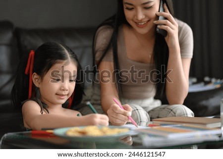 Smiling cute little girl drawing picture near her working mother at home