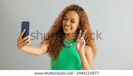 Happy woman, peace sign and selfie with kiss for social media, vlog or memory on a gray studio background. Female person with smile on mobile smartphone for photography or picture on mockup space