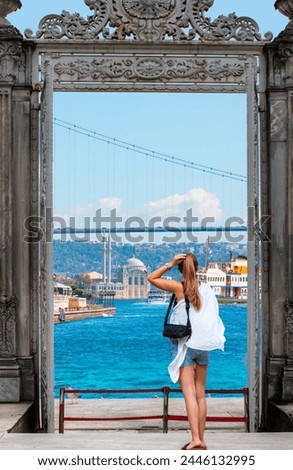 A beautiful blonde girl wearing mini shorts is watching the Bosphorus - The eastern gate of the Dolmabahce Palace on the shores of the Bosphorus with Ortakoy mosque