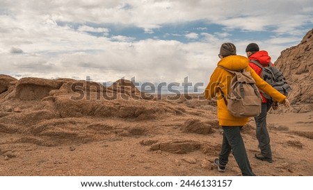 Friends tourists walk along the sandy mountains against the background of the sky and mountains. Clothing for tourism. People are walking through the mountains.