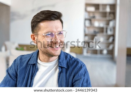 A contented man with a cheerful countenance looks away, his casual attire blending with the soft-hued, modern decor.

 Royalty-Free Stock Photo #2446139343