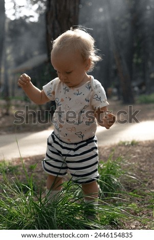 adorable little blonde girl playing with grass in the forest park on a hot sunny day